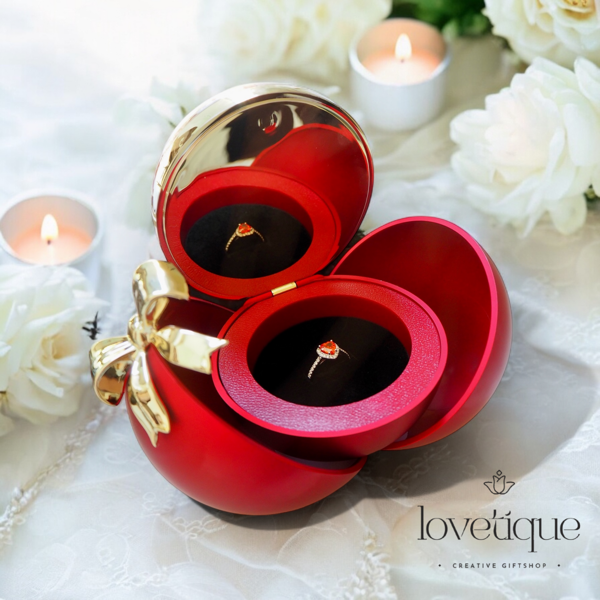 Red jewelry box with gold bow and rings, surrounded by white flowers and candles, featuring 'lovetique' brand.