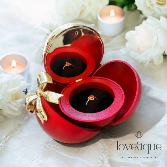 Red jewelry box with gold bow and rings, surrounded by white flowers and candles, featuring 'lovetique' brand.